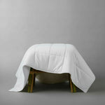 White quilt draped over a wooden stool on a gray background