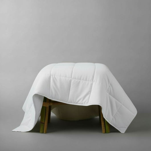 White quilt draped over a wooden stool on a gray background